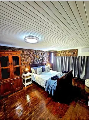 a bedroom with a bed and a wooden floor at Luxury GuesthouseCo FlintstoneHouse in Marloth Park