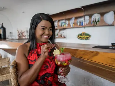 a woman sitting at a bar holding a drink at ANEW Hotel & Convention Centre OR Tambo Johannesburg in Benoni