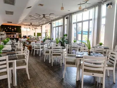 a restaurant with white tables and chairs and windows at ANEW Hotel & Convention Centre OR Tambo Johannesburg in Benoni