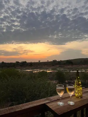 a bottle of wine and two glasses on a wooden table at Croc's Nest Bush Lodge in Marloth Park