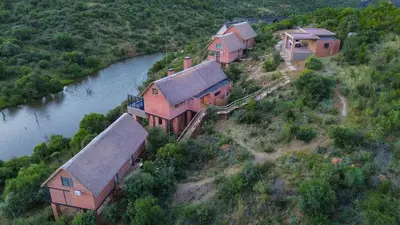 a group of houses on a hill next to a river at Cliffhanger Lodge in Mabula