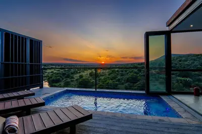a swimming pool with a sunset in the background at Cliffhanger Lodge in Mabula