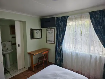 a bedroom with a bed and a desk and a window at King Sanctuary in Centurion