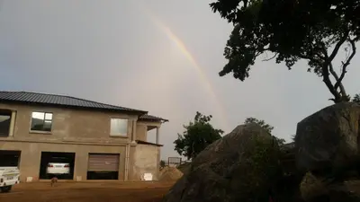 a rainbow over a house with a large rock at Jackal Buzzard Mountain Haven in Hillsowen
