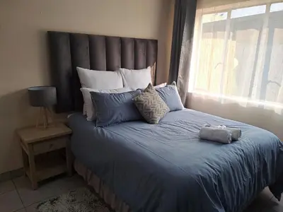 a bed with a blue comforter and a window at Hazel Haven 1 Guest House in Pretoria