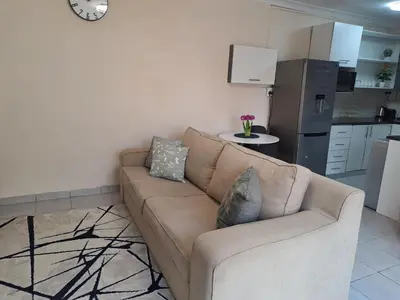 a brown couch in a living room with a kitchen at Hazel Haven 1 Guest House in Pretoria