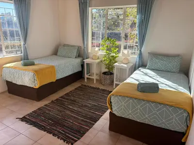 a bedroom with two beds and two windows at The Seed Pod Guesthouse in Modimolle