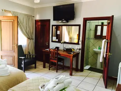 a bedroom with a desk and a bathroom with a mirror at Waterkloof Guest House in Pretoria