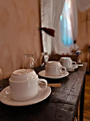 a table with white cups and saucers on it at Die Boskombuis en Gastehuis in Rayton