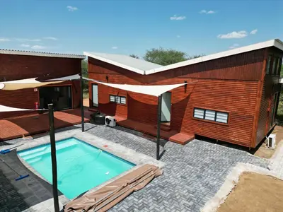 a swimming pool in front of a building with a house at Emintha Log House in Mmukubyane
