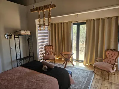 a bedroom with a bed and two chairs and a window at Emintha Log House in Mmukubyane
