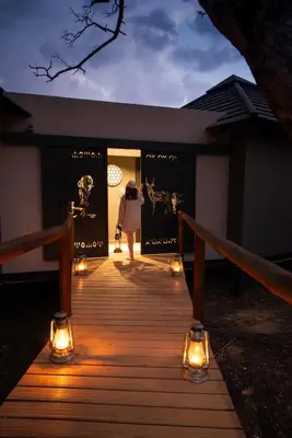 a woman walking down a wooden walkway with lights at Idube Game Reserve in Sabi Sand Game Reserve