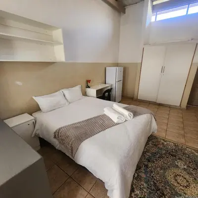 a bedroom with a bed with white sheets and a refrigerator at Sunny Lodge in Pretoria