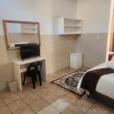 a bedroom with a desk with a computer and a mirror at Sunny Lodge in Pretoria