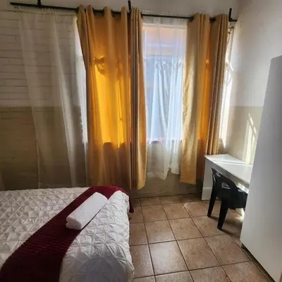a bedroom with a bed and a desk and a window at Sunny Lodge in Pretoria