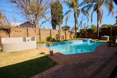 a swimming pool in a yard with a brick wall at Sunny villa with pool and garden in Pretoria