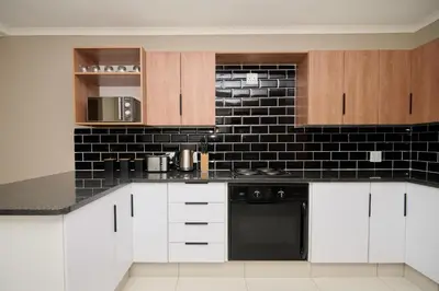 a kitchen with white cabinets and a black tile wall at Sunny villa with pool and garden in Pretoria