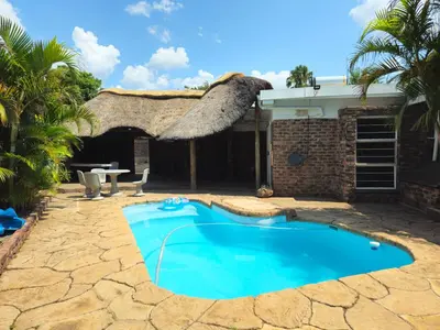 a house with a swimming pool and a thatch roof at Light House Lodge in Bela-Bela