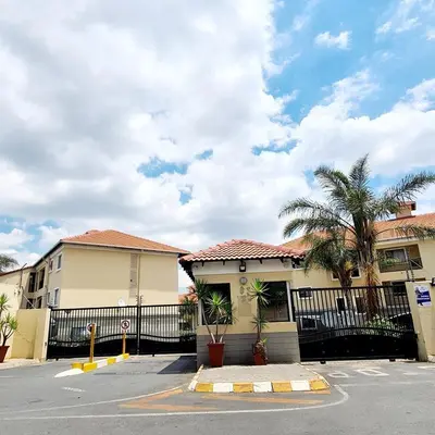 a building with a fence and palm trees in a parking lot at Oasis Home in Midrand