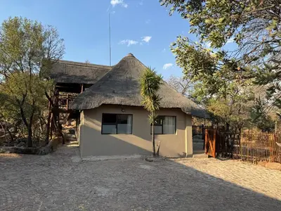 a small building with a thatched roof with a tree at Mbekka Lodge, Mabalingwe in Moheme