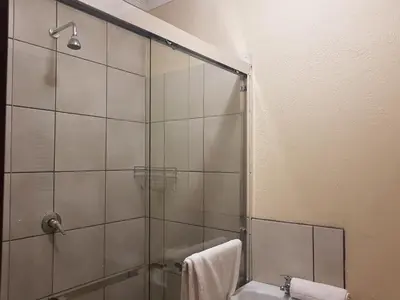 a bathroom with a shower and a toilet and a sink at Sand River Cottages in Hazyview