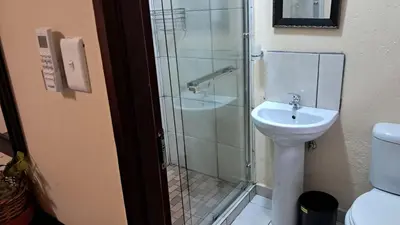 a bathroom with a shower and a sink and a toilet at Sand River Cottages in Hazyview