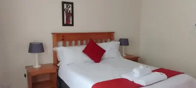 a bedroom with a bed with red and white pillows at Sand River Cottages in Hazyview