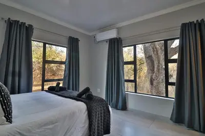 a bedroom with a bed and two large windows at Kruger Stories at Marloth in Marloth Park