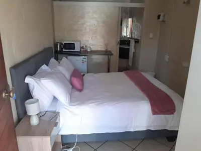 a bedroom with a bed with white sheets and red pillows at Tranquilo Guesthouse in Ermelo