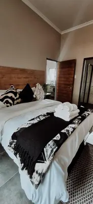 a large bed with a black and white blanket on it at Lazél Apartments in Ermelo