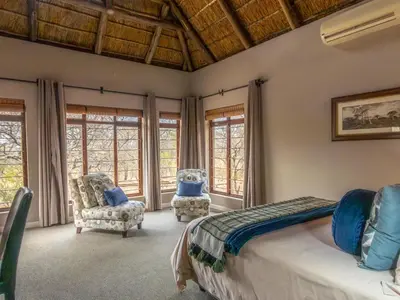a bedroom with a bed and two chairs and windows at Zebula Golf and Wildlife Estate - Africa Breathing Pax 8 - Moi Signature Exclusive Villa in Mabula