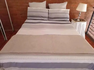 a large bed with white and gray sheets and a lamp at Calswald's Skyline Sanctuary in Midrand
