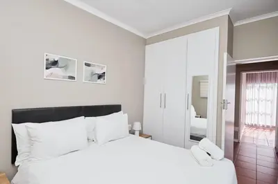 a white bedroom with a white bed and a mirror at Cozy Apartment close to Menlyn in Pretoria