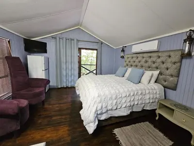 a bedroom with a large bed and a chair at Whispering Creek Mountain Lodge in Magoebaskloof