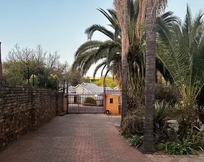 a driveway with a gate with palm trees and a fence at Serene Stays Elarduspark in Pretoria