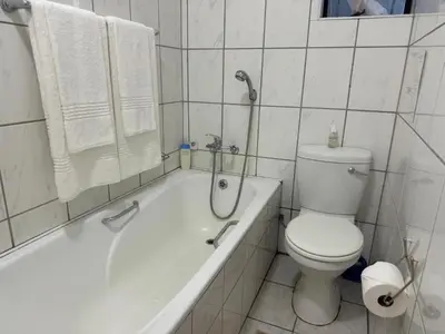 a white bathroom with a toilet and a bath tub at Busa House - Triple Room in White River