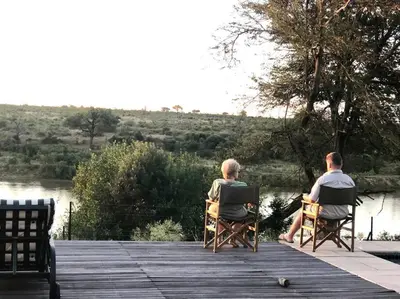 two people sitting in chairs on a wooden dock at Beautiful Home Mjejane Private Game Reserve in Hectorspruit