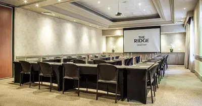 a conference room with tables and chairs and a screen at The Ridge Hotel in Witbank