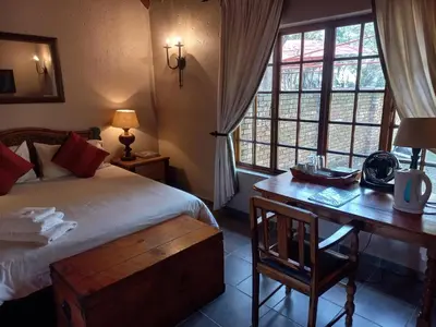a bedroom with a bed and a desk and windows at Khaya Africa Guesthouse in Midrand