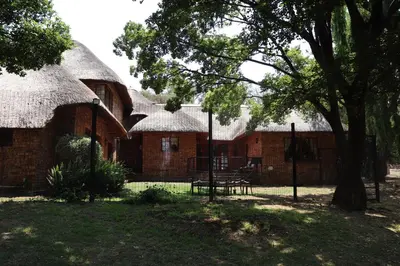 a building with thatched roofs with a picnic table in front at Khaya Africa Guesthouse in Midrand