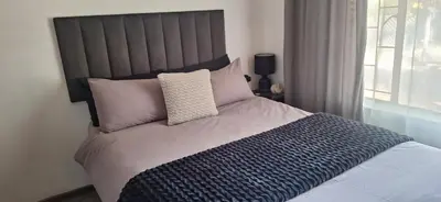 a bedroom with a large bed with pink and blue pillows at Sandgrouse Guesthouse in Centurion