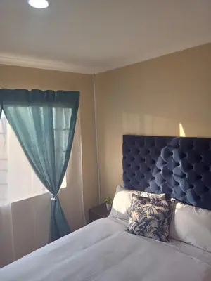 a bedroom with a bed with a blue headboard and a window at Tranquil heights Inn in Centurion