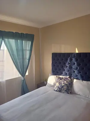 a bedroom with a bed with a blue headboard and a window at Tranquil heights Inn in Centurion