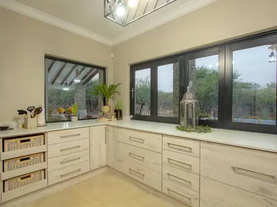 a kitchen with wooden cabinets and large windows at Edjami Lodge in Marloth Park