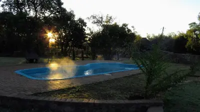a swimming pool in a yard with the sun setting at Modubu Lodge in Bela-Bela