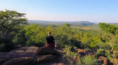 a man sitting on a rock looking out at the mountains at Modubu Lodge in Bela-Bela