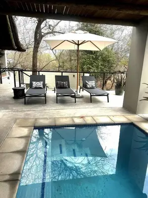 two chairs and an umbrella next to a swimming pool at Bateleur Kruger Lodge in Marloth Park