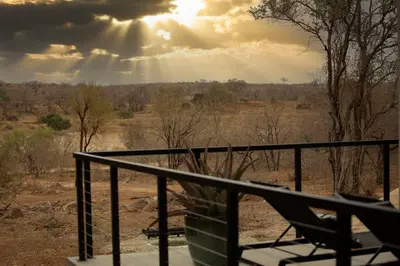 a balcony with a chair and the sun in the sky at Bateleur Kruger Lodge in Marloth Park
