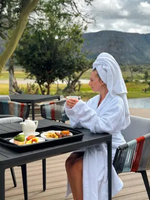 a woman sitting at a table with a plate of food at Honeyguide Conservation Lodge in Golders Green