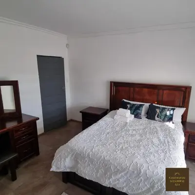a bedroom with a white bed with a wooden headboard at Kanyamazane Guesthouse 1214 in eNyamazaneni
